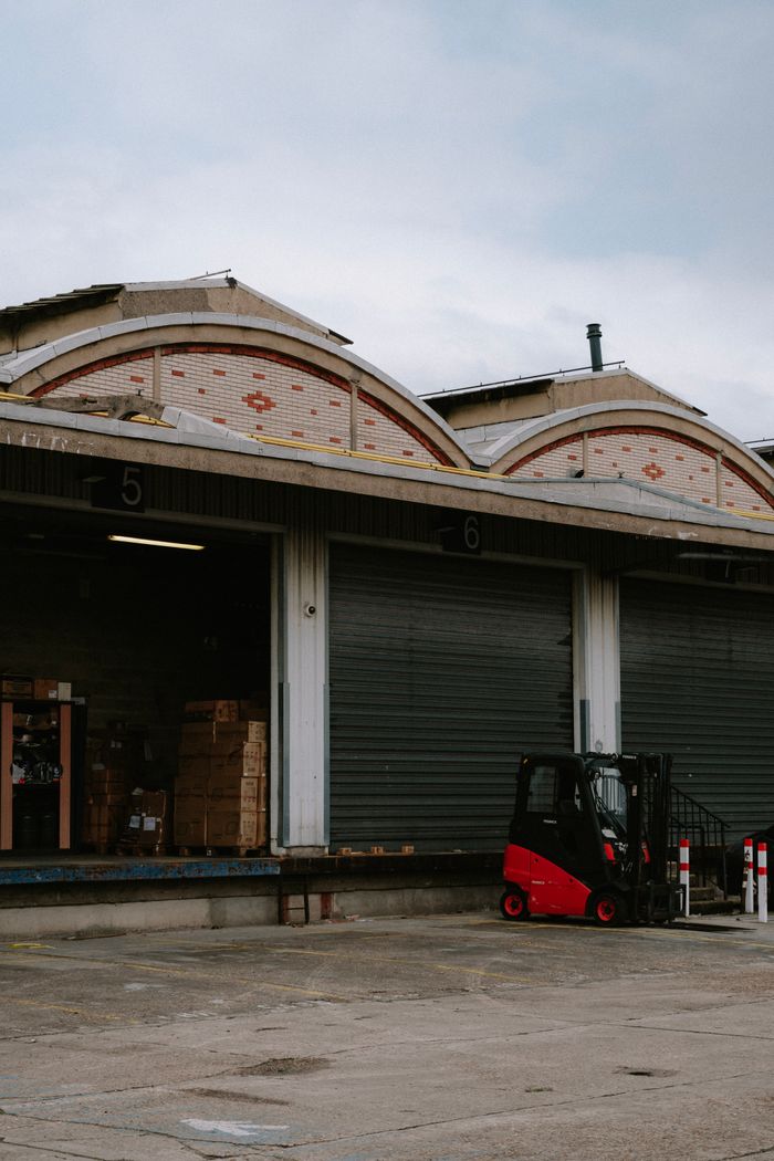 gallery-2 A red forklift parked at a warehouse loading dock with closed garage doors.