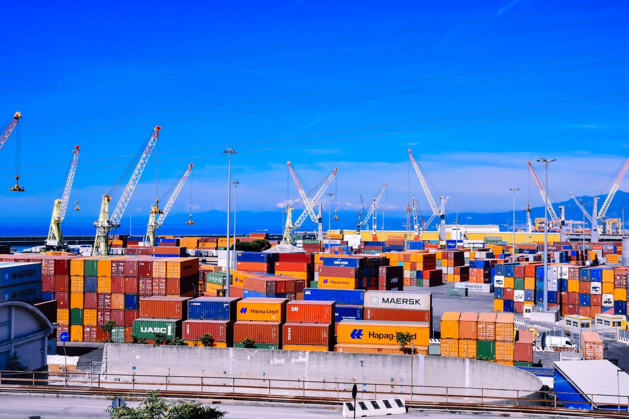 hero-img-02 A bustling shipping port with colorful stacked containers and numerous cranes under a clear blue sky.