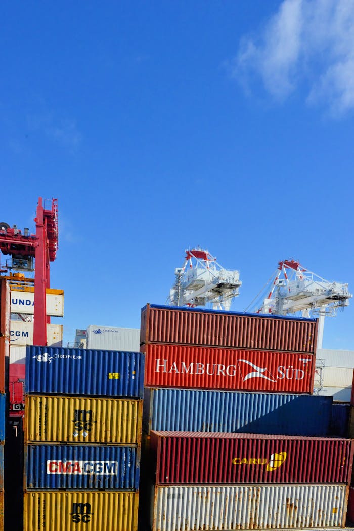 gallery-1 Colorful cargo containers stacked at a busy shipping port under a clear blue sky.