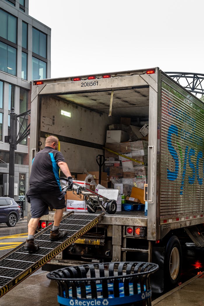 A man loads packages into a delivery truck in a modern urban area.