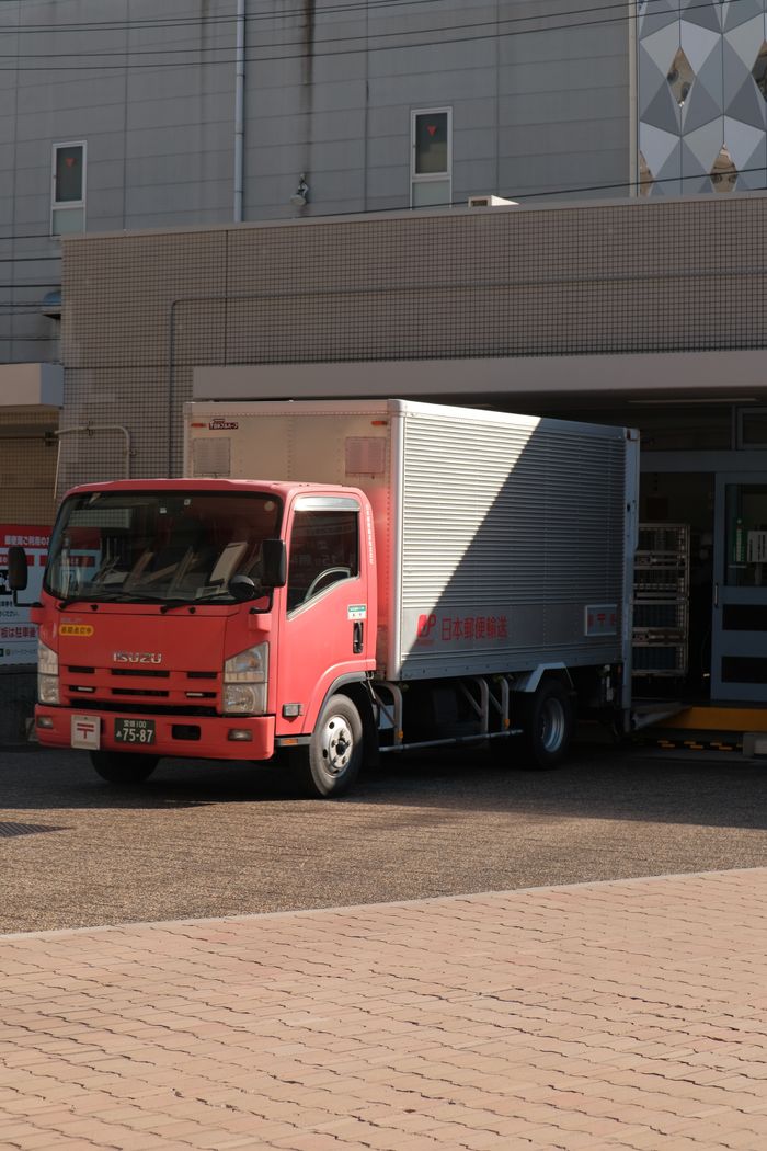 services-01 A red delivery truck unloading goods at a warehouse on a sunny day in the city.