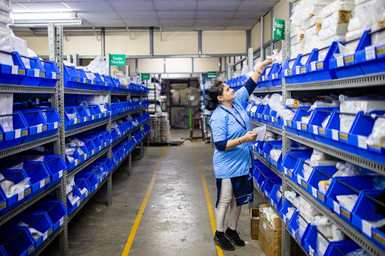 services-img Woman in uniform organizing inventory in a warehouse aisle with labeled bins.