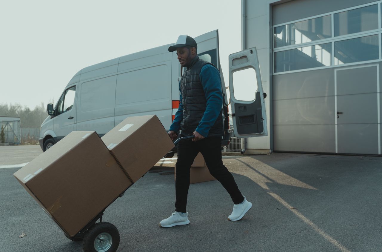 gallery-5 Courier pushing a trolley with boxes near a van at a warehouse, showcasing delivery services.