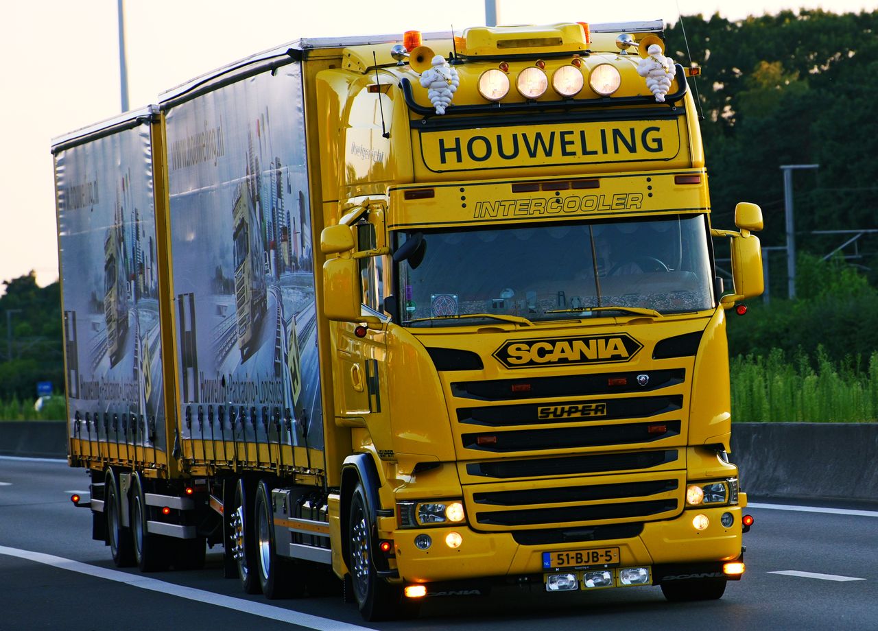 A vibrant yellow Scania truck with 'Houweling' branding driving on a highway.