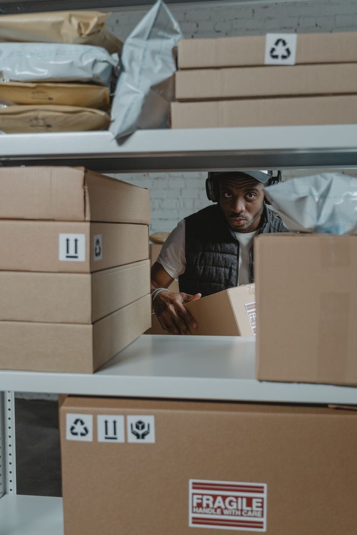 Man organizing packages on shelves in a warehouse setting with cardboard boxes.